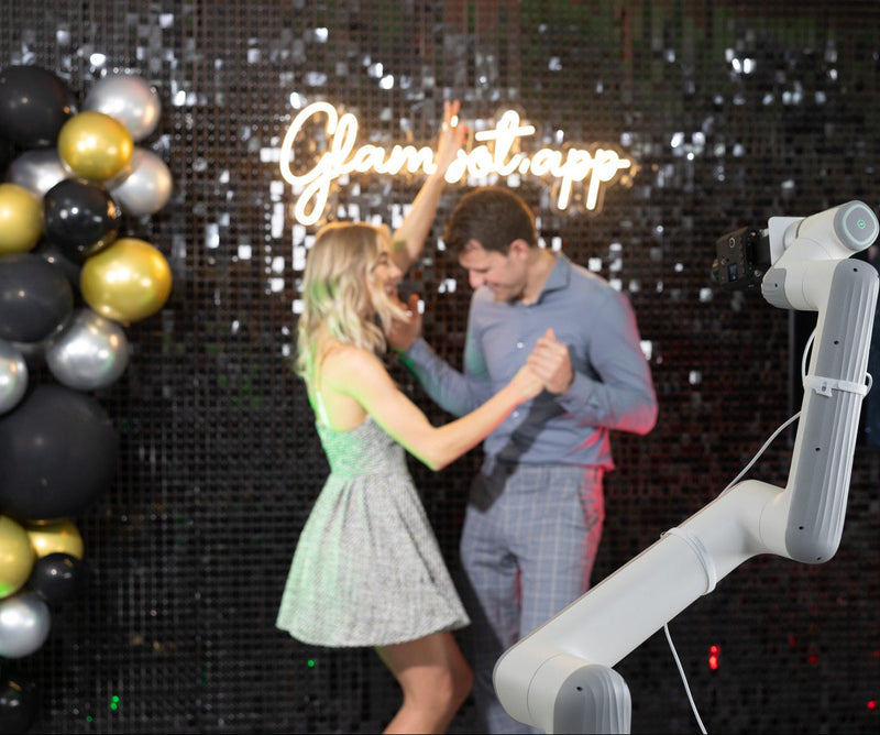 Robotic arm dancing with a person at a party with balloons and 'Ola!舞会' sign.